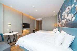 A modern hotel room with a large bed, a flat-screen TV mounted on the wall, a small round table, and a painting of flowers on the wall. - Magnotel (Qinzhou)