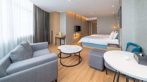A modern hotel room with a bed, a sofa, a small table, and a TV. - Magnotel (Qinzhou)