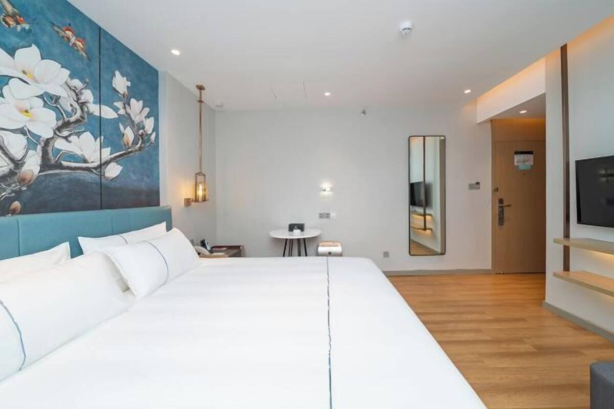 A modern hotel room with a large bed, a painting of flowers on the wall, a small table, and a TV mounted on the wall.