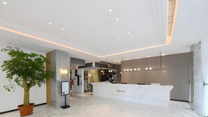A modern reception area with a marble floor, a reception desk, a potted plant, and a digital information board. - Magnotel (Qinzhou)