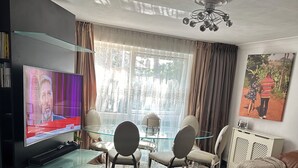 A modern living room with a flat-screen TV, glass coffee table, and leather sofa. - Charming Flat in North London (London)