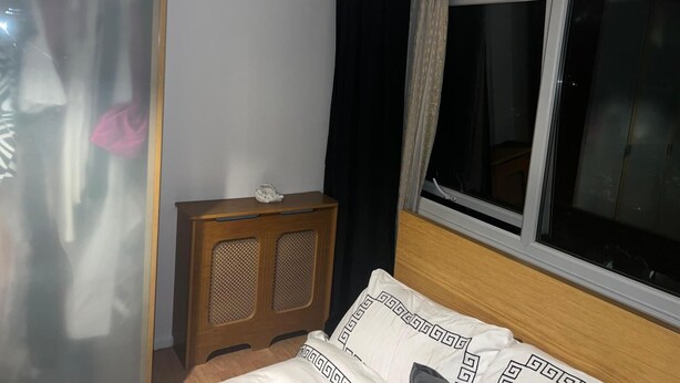 A bedroom with a bed, a wooden nightstand, a window with curtains, and a wardrobe. - Charming Flat in North London (London)