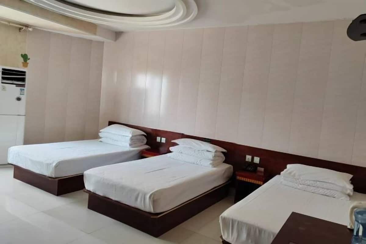 A hotel room with two single beds, a wooden headboard, a small table, and a wall-mounted air conditioner.