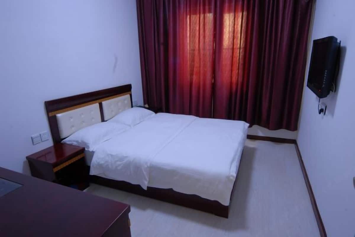 A single bed with a wooden headboard, a bedside table, and a wall-mounted TV.