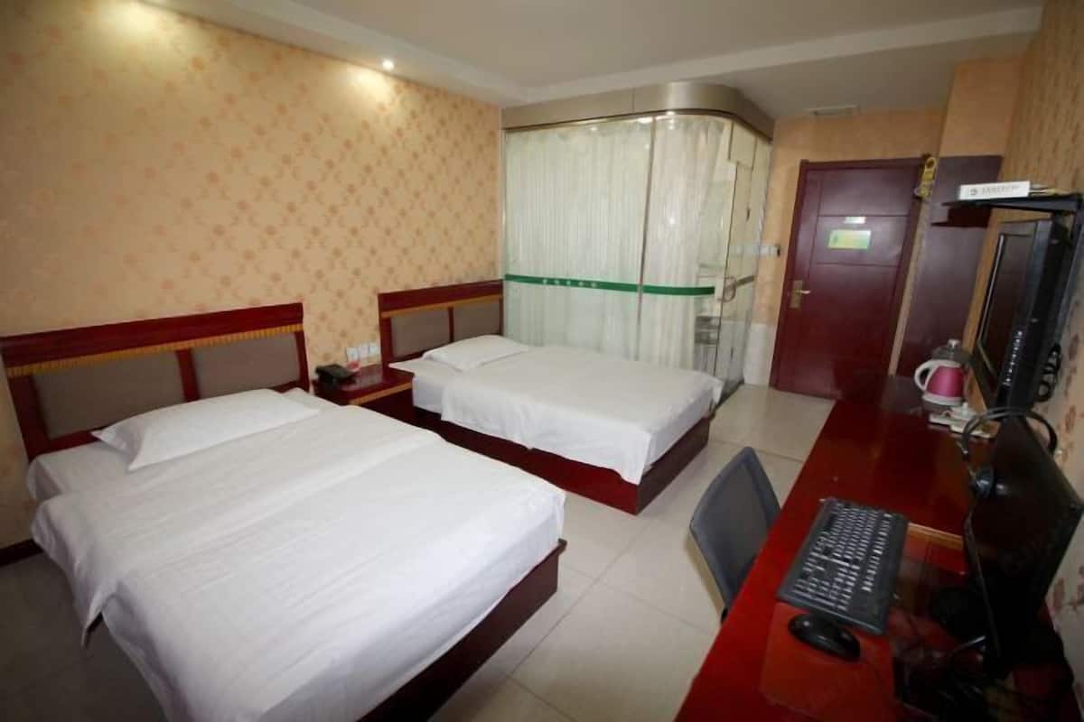 A hotel room with two beds, a desk with a computer, and a shower area.
