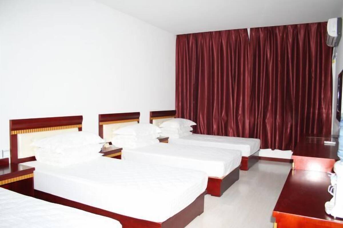 A hotel room with three single beds, a wooden headboard, a large mirror, and a red curtain.