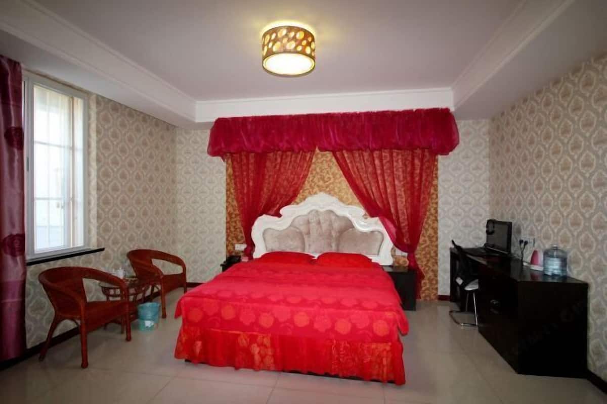 A bedroom with a bed, a desk, two chairs, a nightstand, and a lamp.