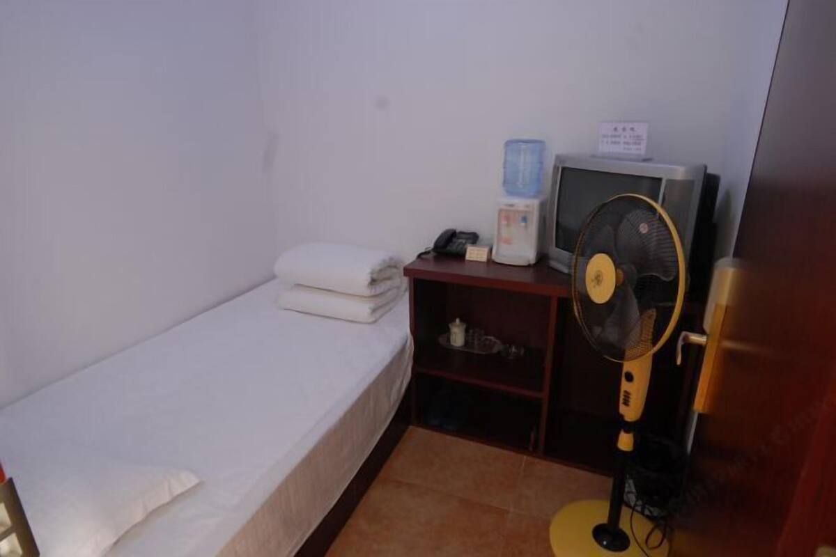 A small room with a single bed, a desk with a computer and a fan, and a water dispenser.