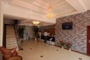 Un hall de hotel con una recepción, una escalera y un candelabro.