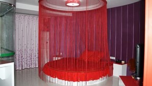 Ein Zimmer mit einem runden Bett, einer Glastrennwand, einem Fernseher und einer violetten Wand.