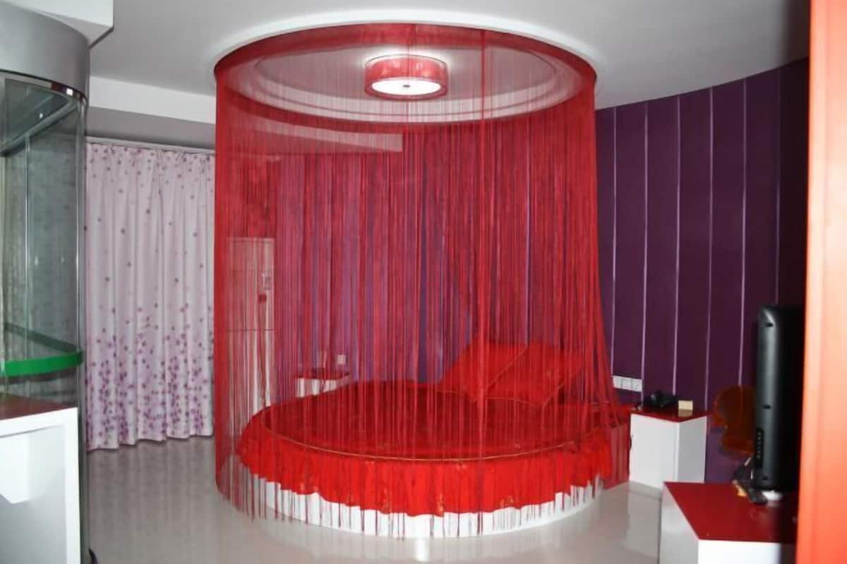 A circular bed with a red canopy, a television on a stand, and a purple wall.