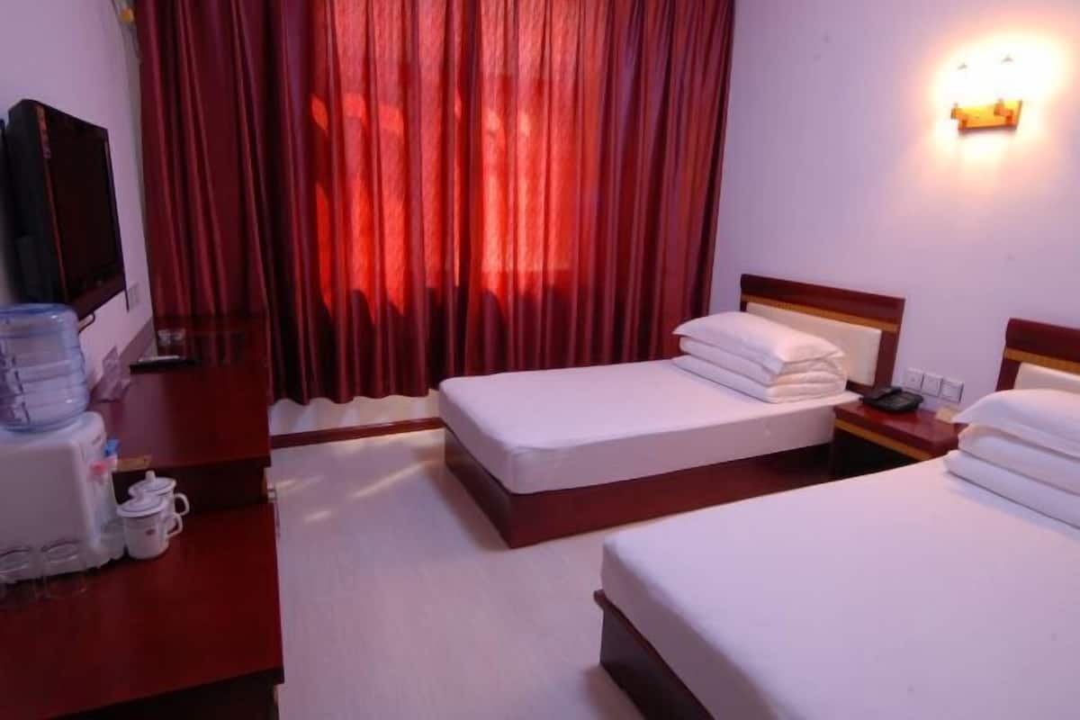 A hotel room with two beds, a TV, a water dispenser, and a wall-mounted light.