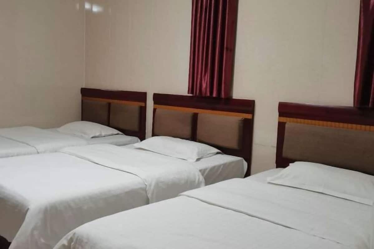 A hotel room with three single beds, each with a wooden headboard and white bedding.