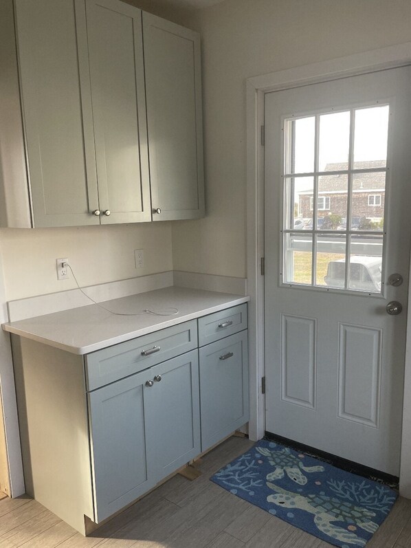 A kitchen with light gray cabinets, a white countertop, and a door with a window.