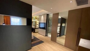 A modern hotel room with a wooden floor, a large mirror, a television, and a sliding door leading to a bathroom. - Shuiyi Boqing Hotel (Heze)