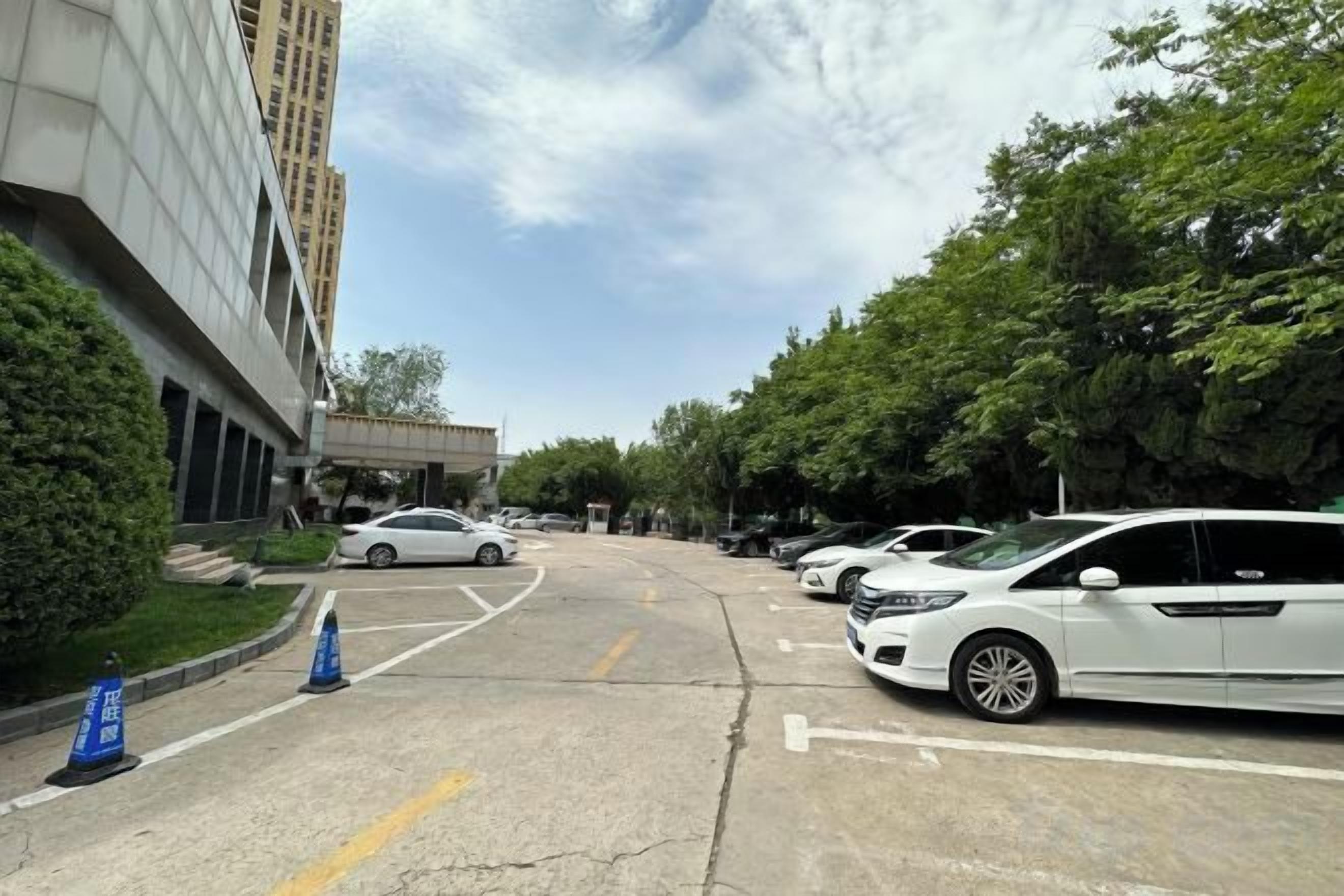 Un estacionamiento con coches, un edificio a la izquierda y árboles a la derecha.