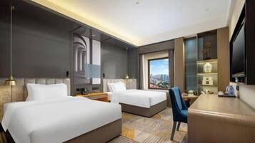 Hotelkamer met twee bedden, een bureau, een stoel, een televisie en een groot raam met uitzicht op de stad.