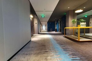 Un pasillo de hotel con piso alfombrado, un mostrador de recepción con una planta y una zona alfombrada azul.