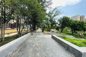 Un sendero pavimentado bordeado de árboles y follaje, que conduce a una zona verde con un banco.
