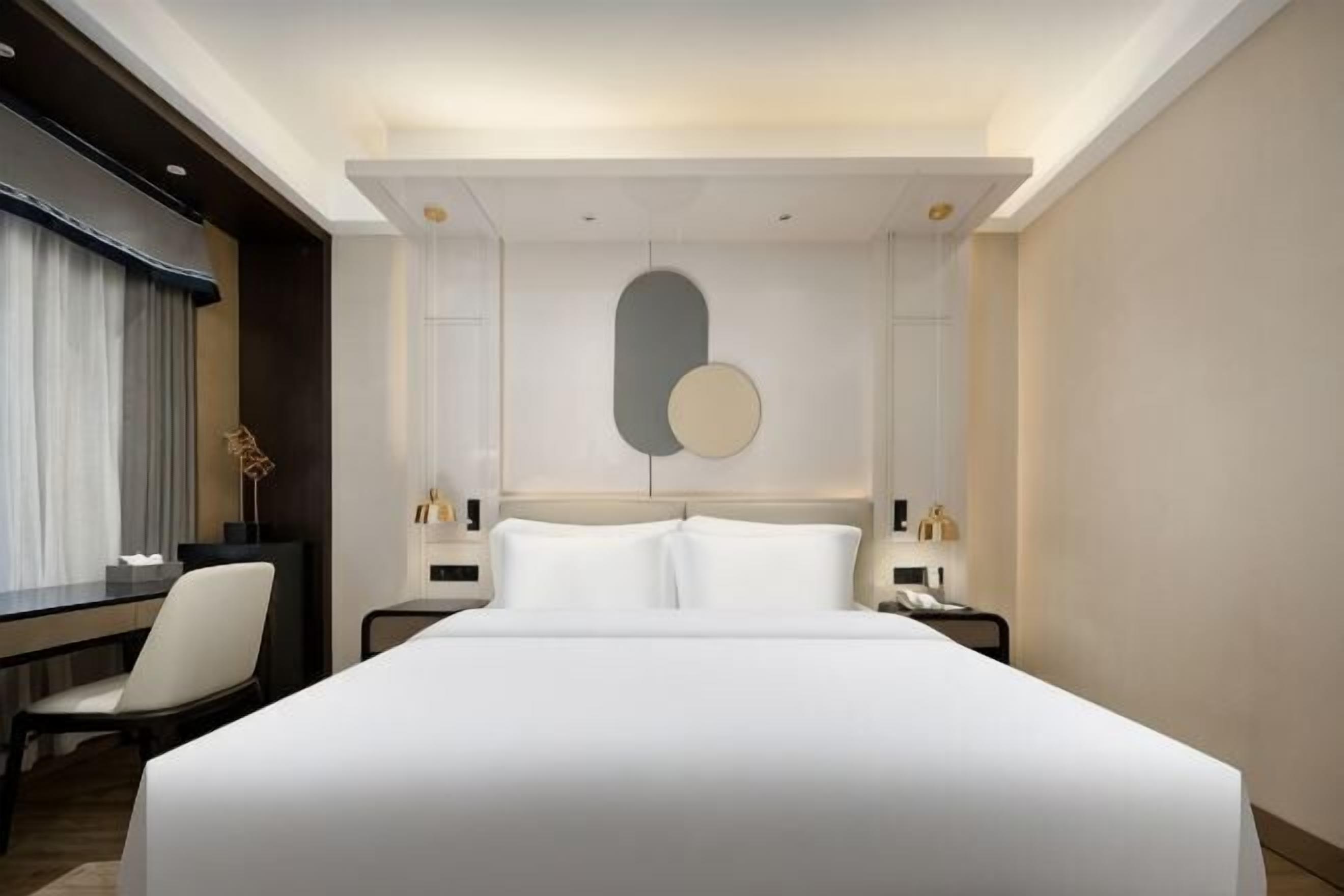 A hotel room with a large bed, bedside tables, a desk, and a chair.