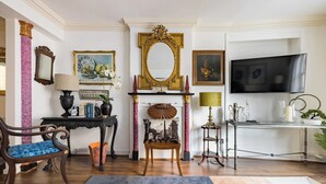 A room with a fireplace, a television, a desk with a lamp, and a chair.