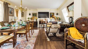 A dining room with a wooden table set for a meal, surrounded by chairs. There is a sofa and a decorative armchair with a yellow throw.