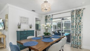 A dining area with a wooden table, blue chairs, and blue placemats. There is a potted plant on the table, and a ceiling light fixture above. - Your vacation home away from home (Naples)