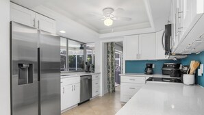A modern kitchen with stainless steel appliances, white cabinetry, and a blue accent wall. - Your vacation home away from home (Naples)
