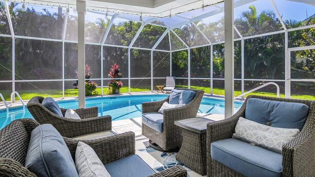 A covered outdoor area with wicker furniture and a pool. - Your vacation home away from home (Naples)