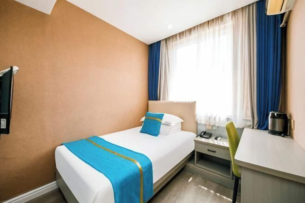 A hotel room with a bed, a desk, a chair, a nightstand, and a window with curtains.