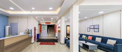 Un vestíbulo de hotel con una recepción, un sofá, una mesa de centro y una escalera al fondo.