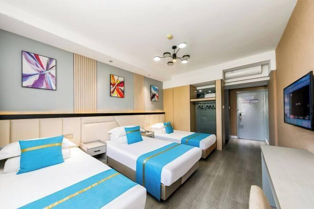 A hotel room with three beds, a TV, and artwork on the walls.