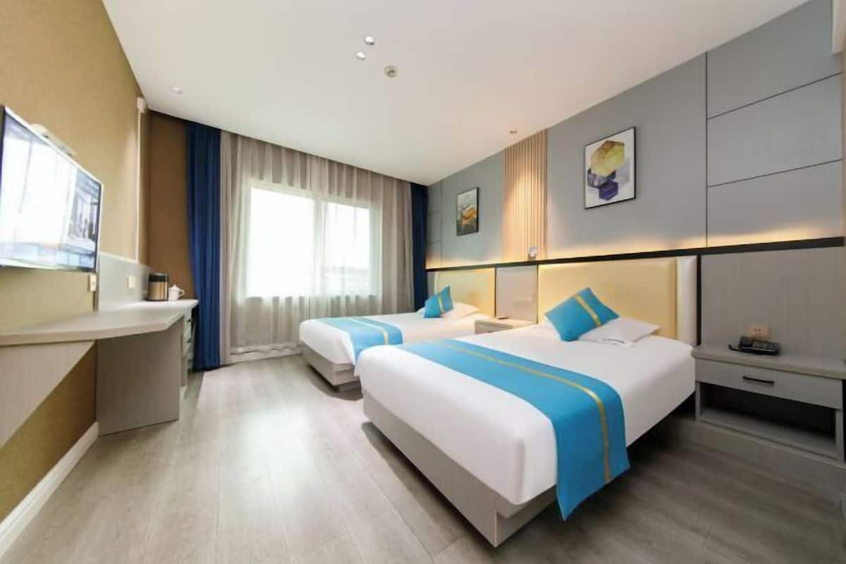 A hotel room with two beds, a desk, a TV, and a window with curtains.