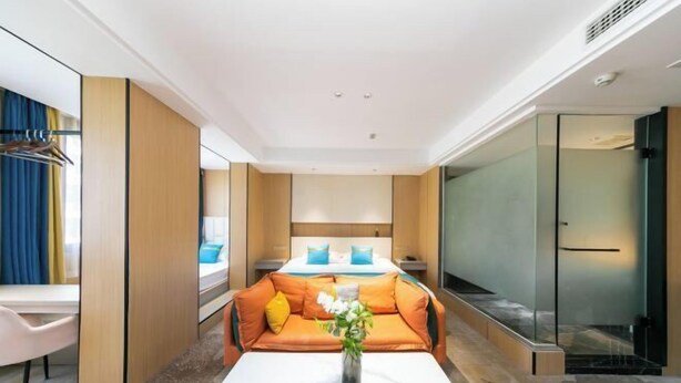 A modern hotel room with a sofa bed, a small table with a vase, a desk, and a glass partition. - Naxiang Fujian Holiday Inn (Zhujiajian branch of Oriental Garden Hotel) (Zhoushan)