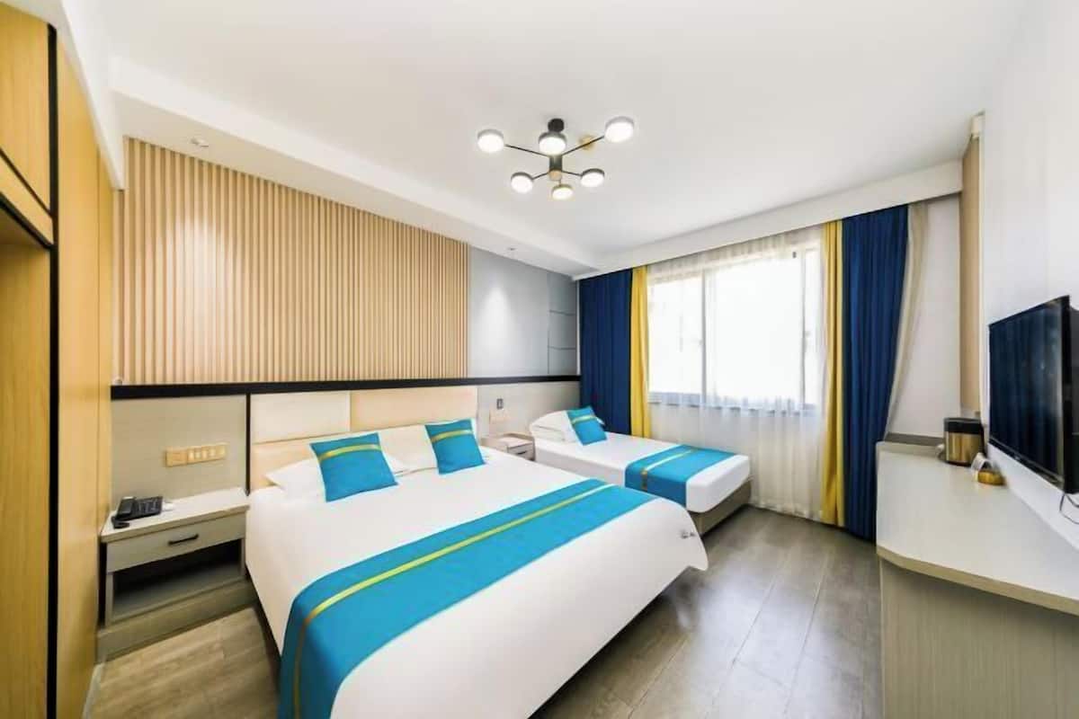 A hotel room with two beds, a TV, a desk, and a window with curtains.