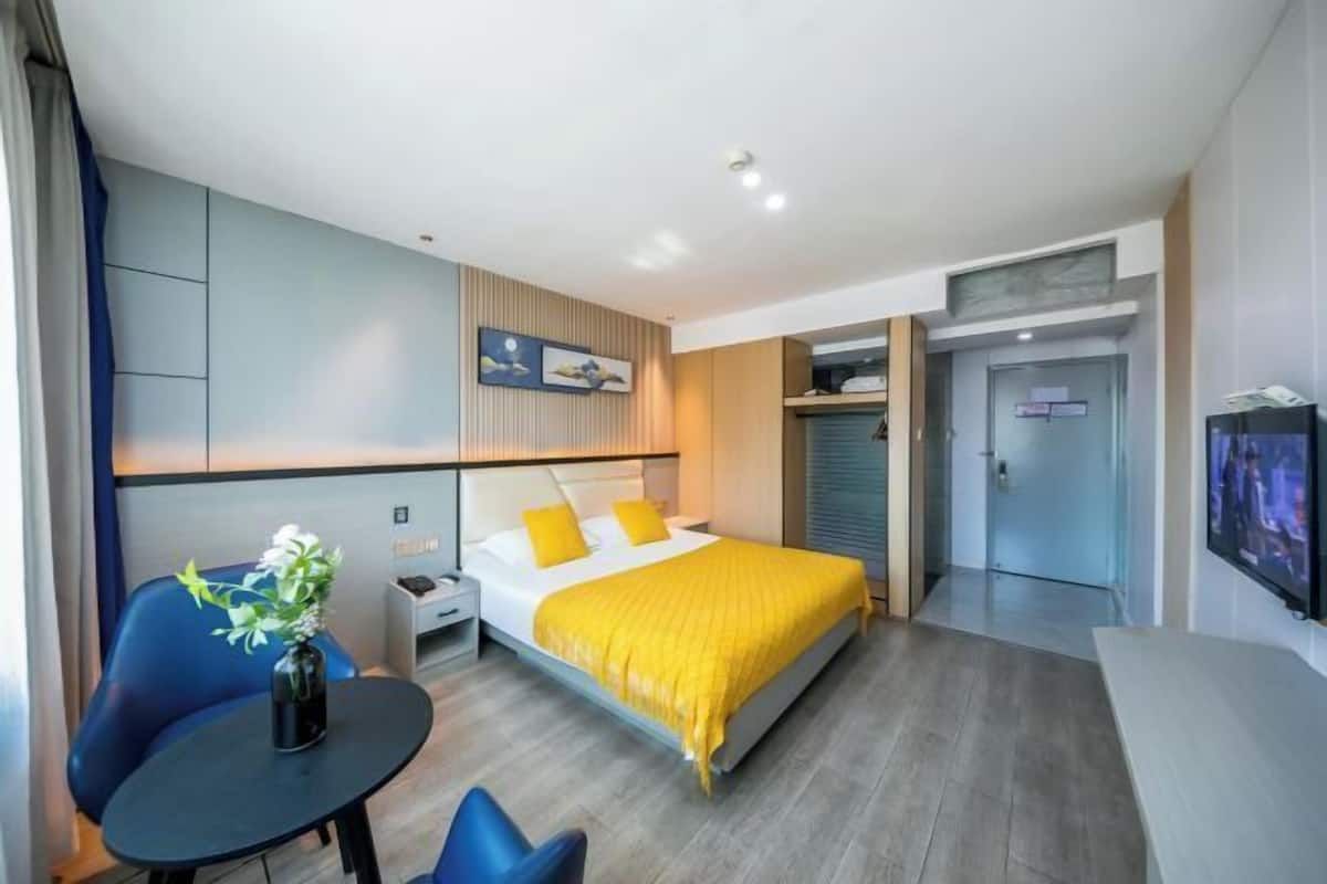 A modern hotel room with a bed, a desk, a chair, a TV, and a door leading to a bathroom.