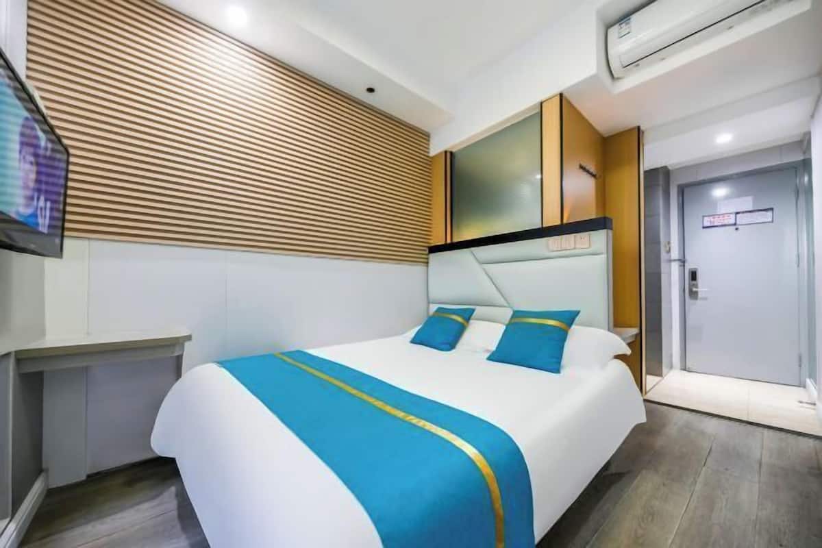 A hotel room with a bed, a TV, a wooden slat wall, a door, and a light switch.