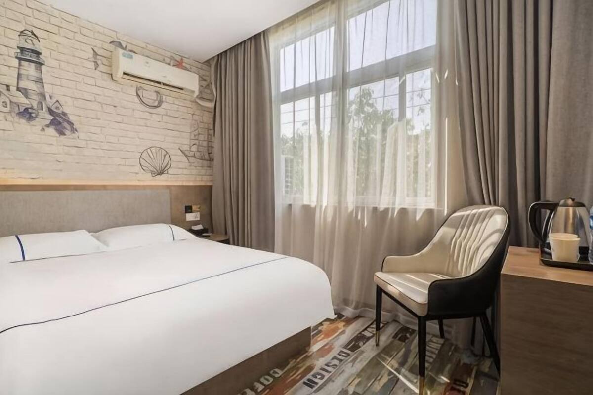 A hotel room with a large bed, a chair, a desk, and a window with curtains.