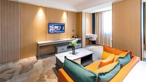 A modern hotel room with a sofa, coffee table, TV, and a desk. - Naxiang Fujian Holiday Inn (Zhujiajian branch of Oriental Garden Hotel) (Zhoushan)
