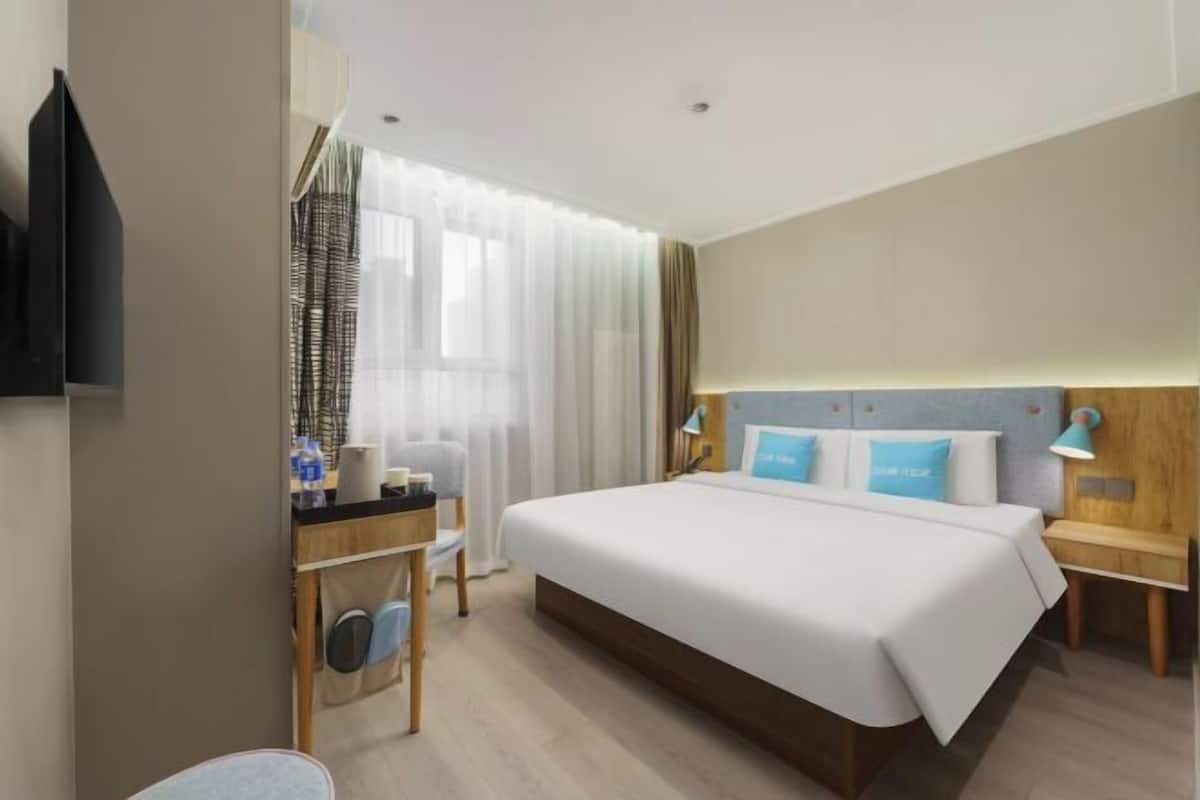 Quarto de hotel com cama, mesas de cabeceira, escrivaninha, cadeira, televisão e janela com cortinas.