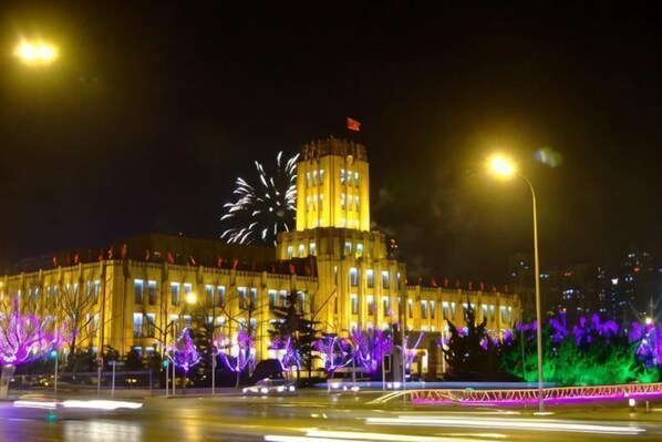 A large building with a prominent tower, illuminated windows, and a flag on top.
