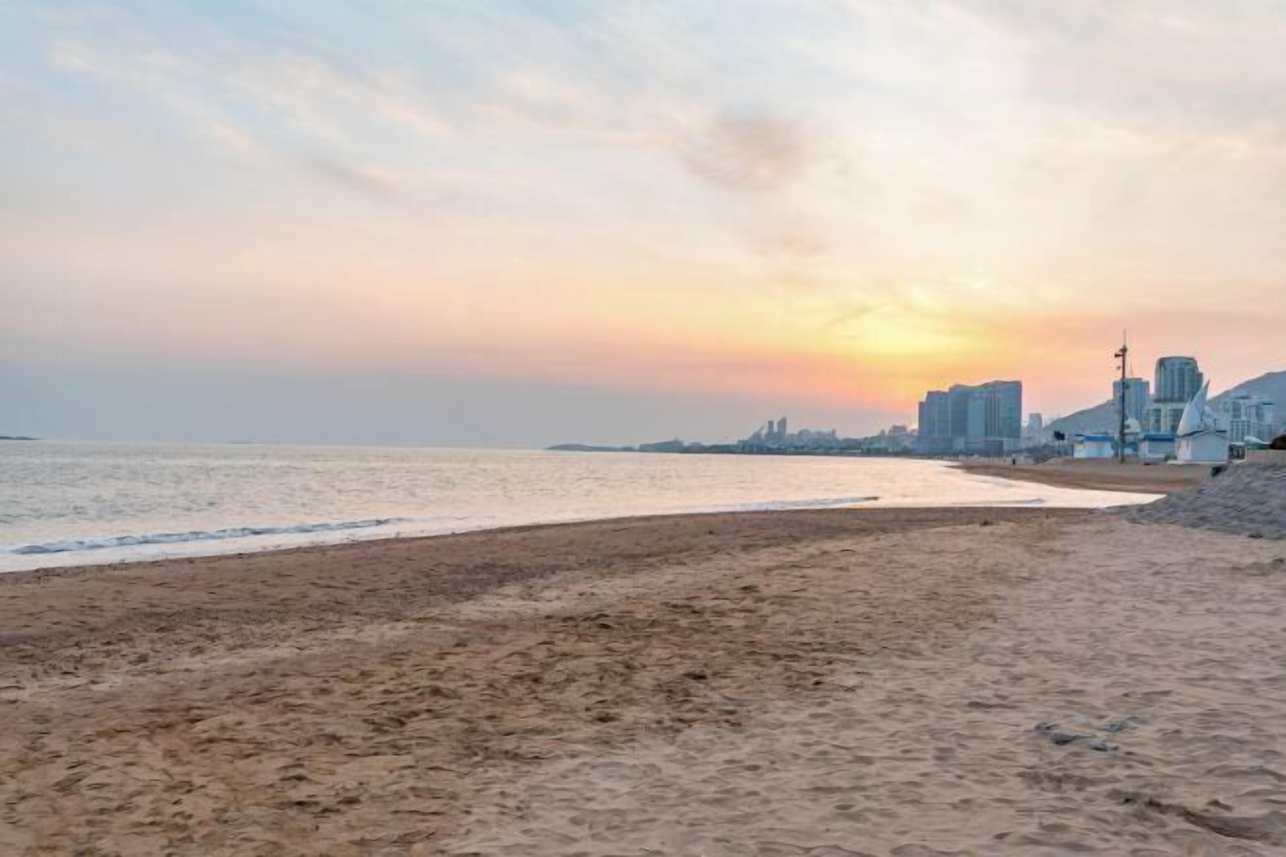 Ein Strand mit Stadtansicht im Hintergrund bei Sonnenuntergang.
