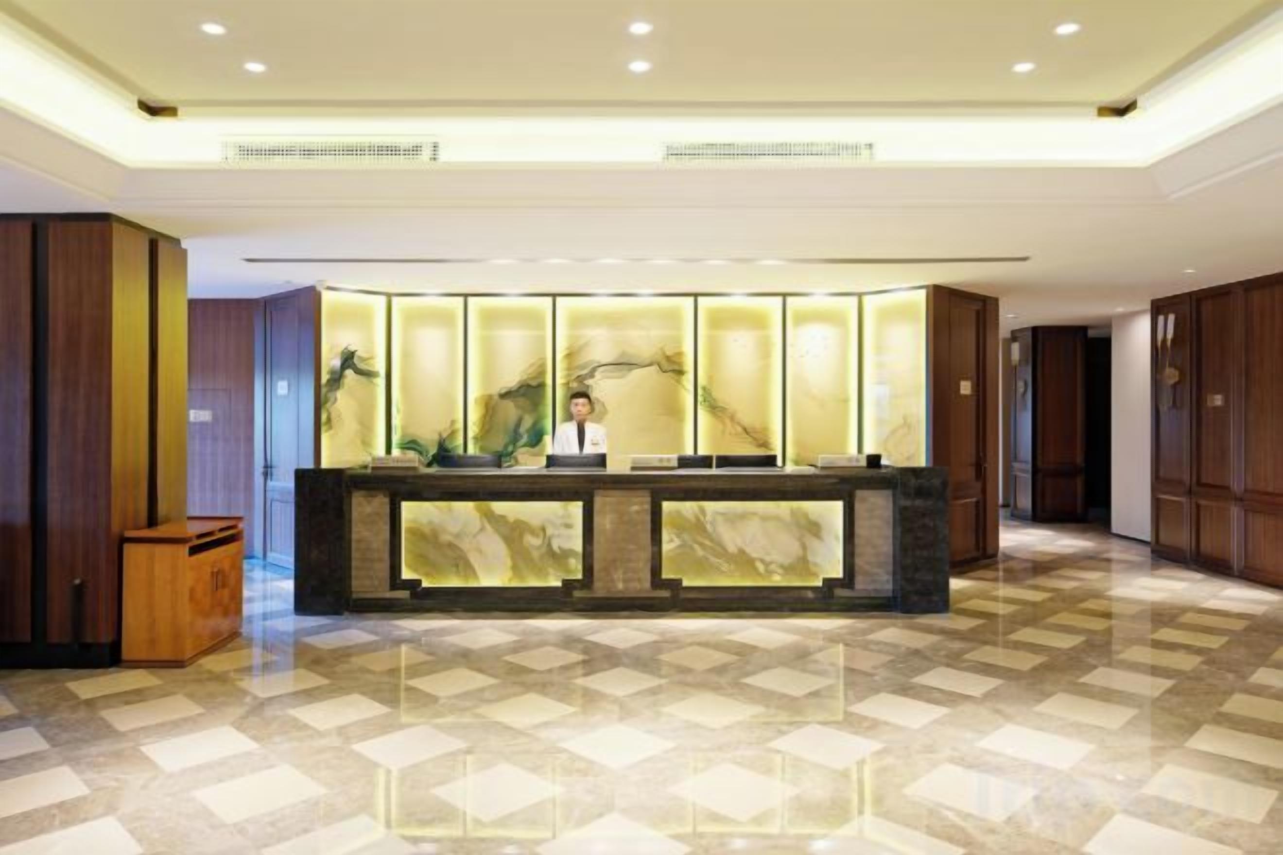 A hotel reception area with a marble counter, a receptionist, and a check-in desk.