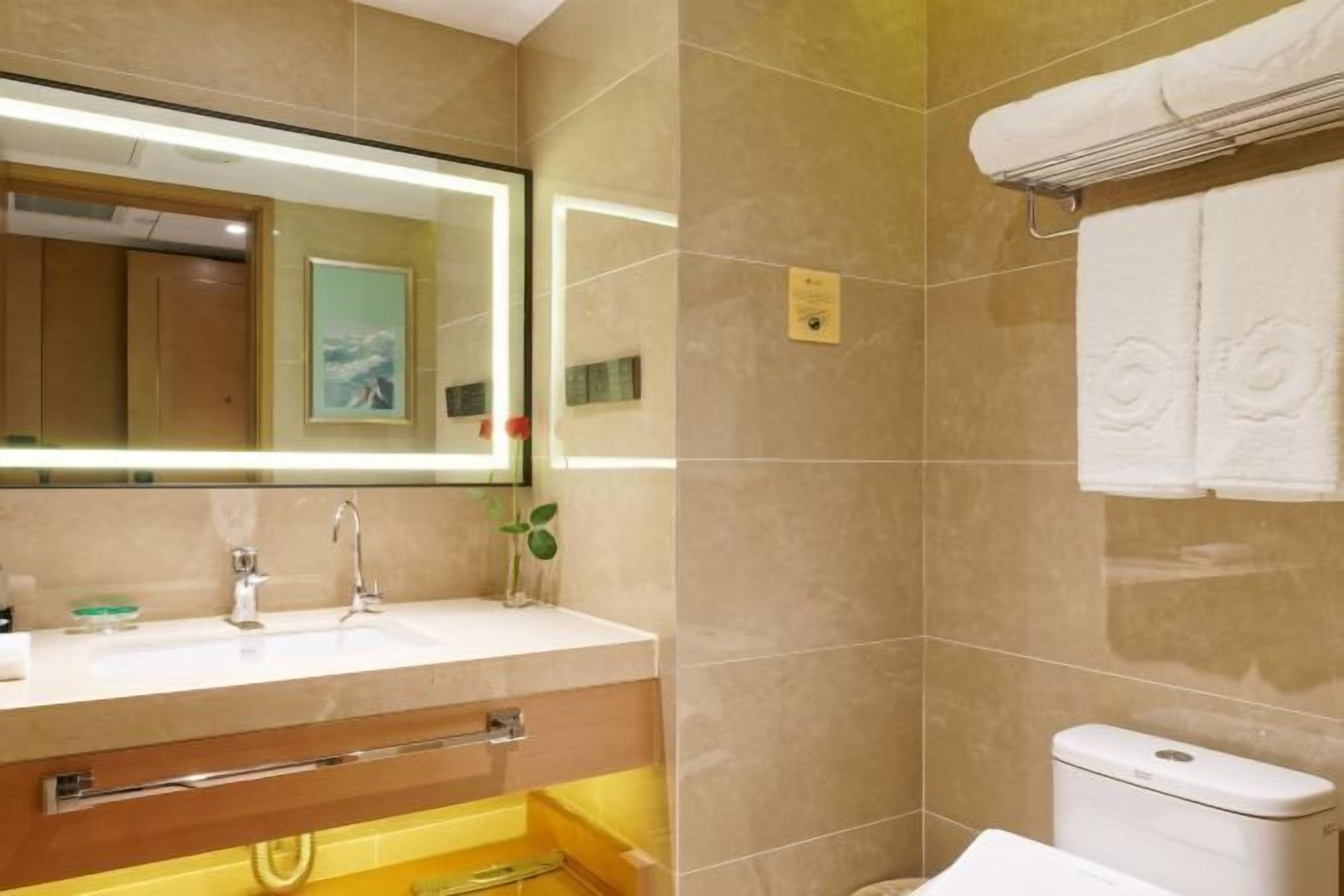 A bathroom with a large mirror, a sink, a toilet, and a towel rack.