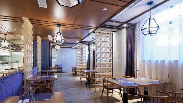 Een restaurant met houten tafels en stoelen, hangende lampen en boekenkasten op de achtergrond.