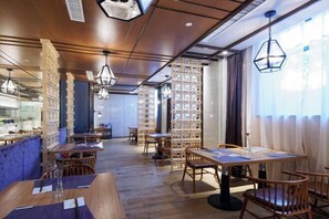 A restaurant with wooden tables and chairs, hanging pendant lights, and bookshelves in the background. - Qingdao Huaxi Hotel (Qingdao)