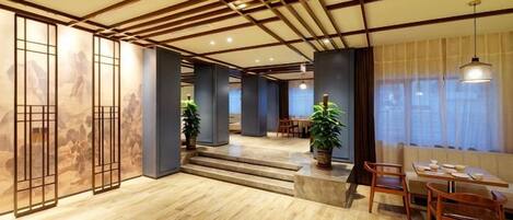 A spacious room with a wooden floor, a dining area with chairs and a table, and a large window with curtains.