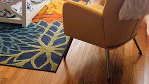 Ein Wohnzimmer mit blauem Sofa, gelben Sessel, Teppich mit Muster und Couchtisch aus Holz.
