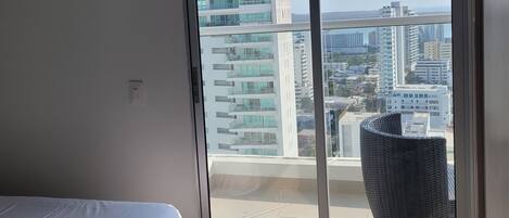 A modern bedroom with a large window, a bed, and a view of a cityscape.