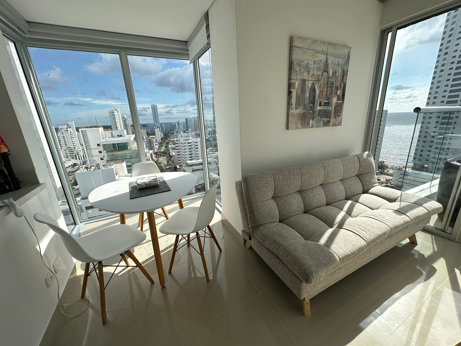 Una sala de estar moderna con un ventanal grande, una mesa redonda blanca, dos sillas blancas y un sofá gris.